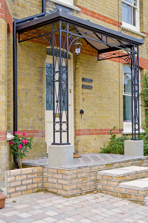 Wrought Iron Deco Design Porch Covered Entrance featuring decorative flower detail stood on Natural Stone Plinths with Cast Iron Shoes and Roof Framework Tongue and Groove Wood Lining and finished in Lead