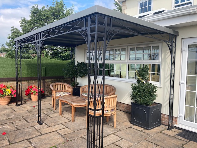 Traditional Trellis Verandah with Spandrel Brackets, Cast Shoe Covers and a curved Glazing Bar Roof Cover with Glass panes over Patio Doors and Windows and Zinc Infill sheets to the remainder creating a shaded outdoor living space 